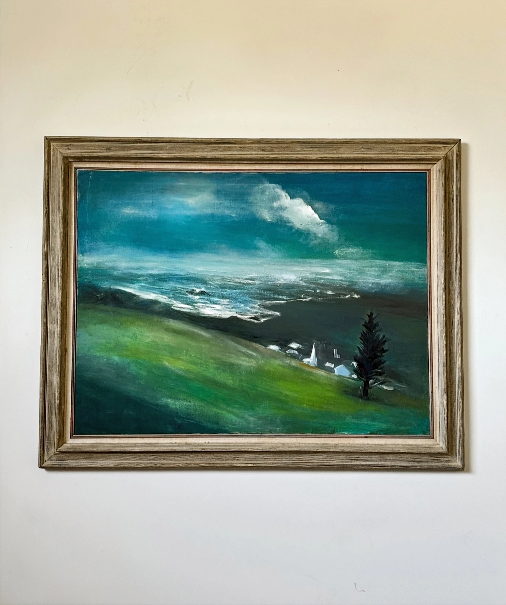 A coastal valley with green hills, dark trees and a small church beneath a sweeping blue and white sky. Church in The Valley, by Evelyn Altman.