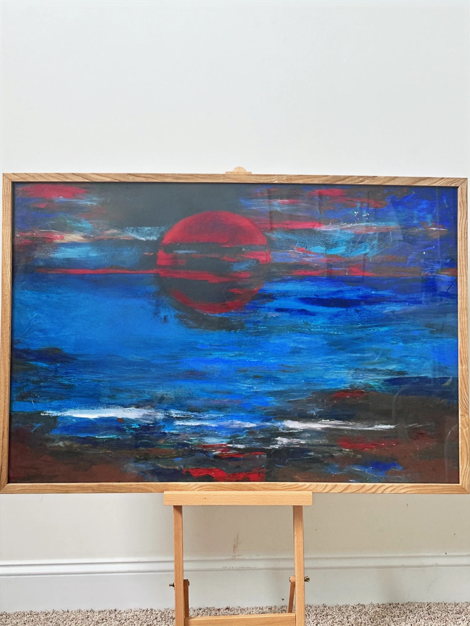 A red sun reflected in broad blue and violet bands of sea above a dark rocky shoreline. Sunset Seaview, by Evelyn Altman.
