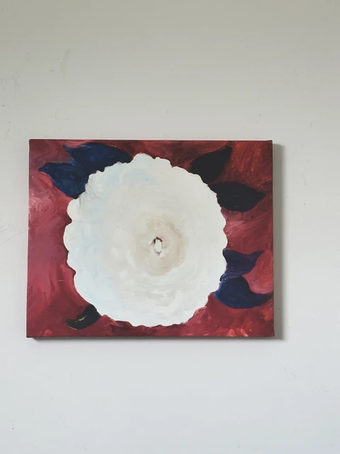 A large white flower surrounded by nearly black leaves on a deep red background. White Flower on Red Background, by Evelyn Altman.