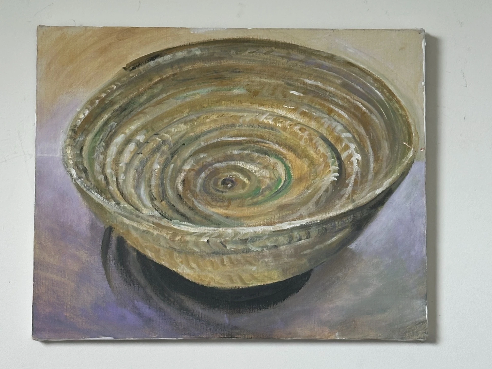 A shallow pottery bowl with concentric olive and gold rings viewed from above on a muted surface. The Study of A Pottery Bowl, by Evelyn Altman.