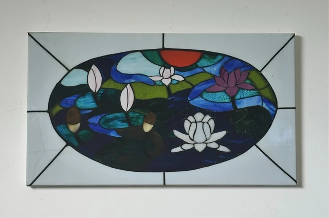 An oval pond of blue water, green lily pads and white flowers divided by dark outlines. Lilies in The Pond, by Evelyn Altman.